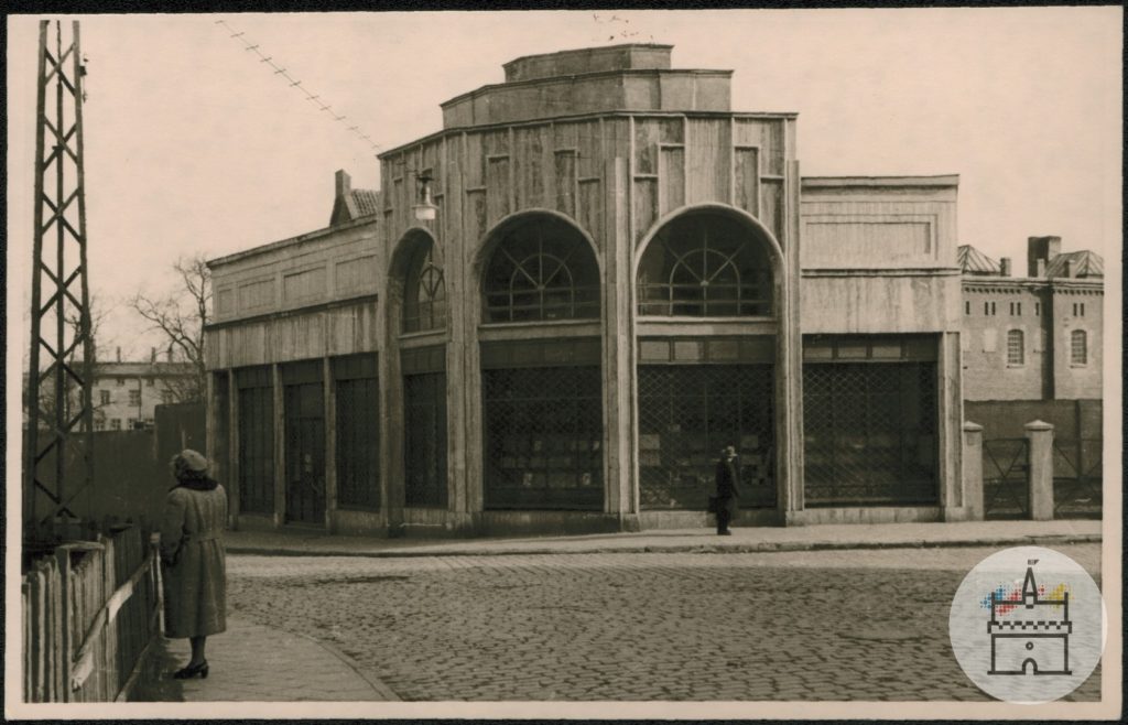 Fotografia przedstawia budynek dawnego Domu Książki na rogu ulic Piłsudskiego i 17 Marca. W tle widać budynek więzienia. Na pierwszym planie kobieta, przy budynku stoi mężczyzna.